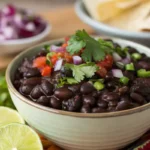 Steaming bowl of Cuban black beans with fresh garnishes.